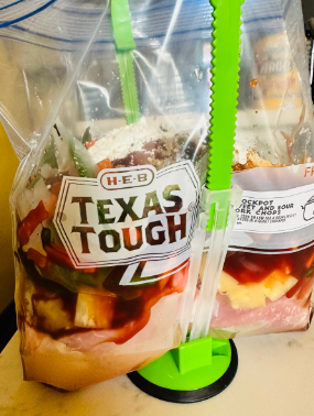 H-E-B Texas Tough bags filled with marinated chicken and vegetables, secured with a bright green sealing tool, placed on a countertop for meal prep.